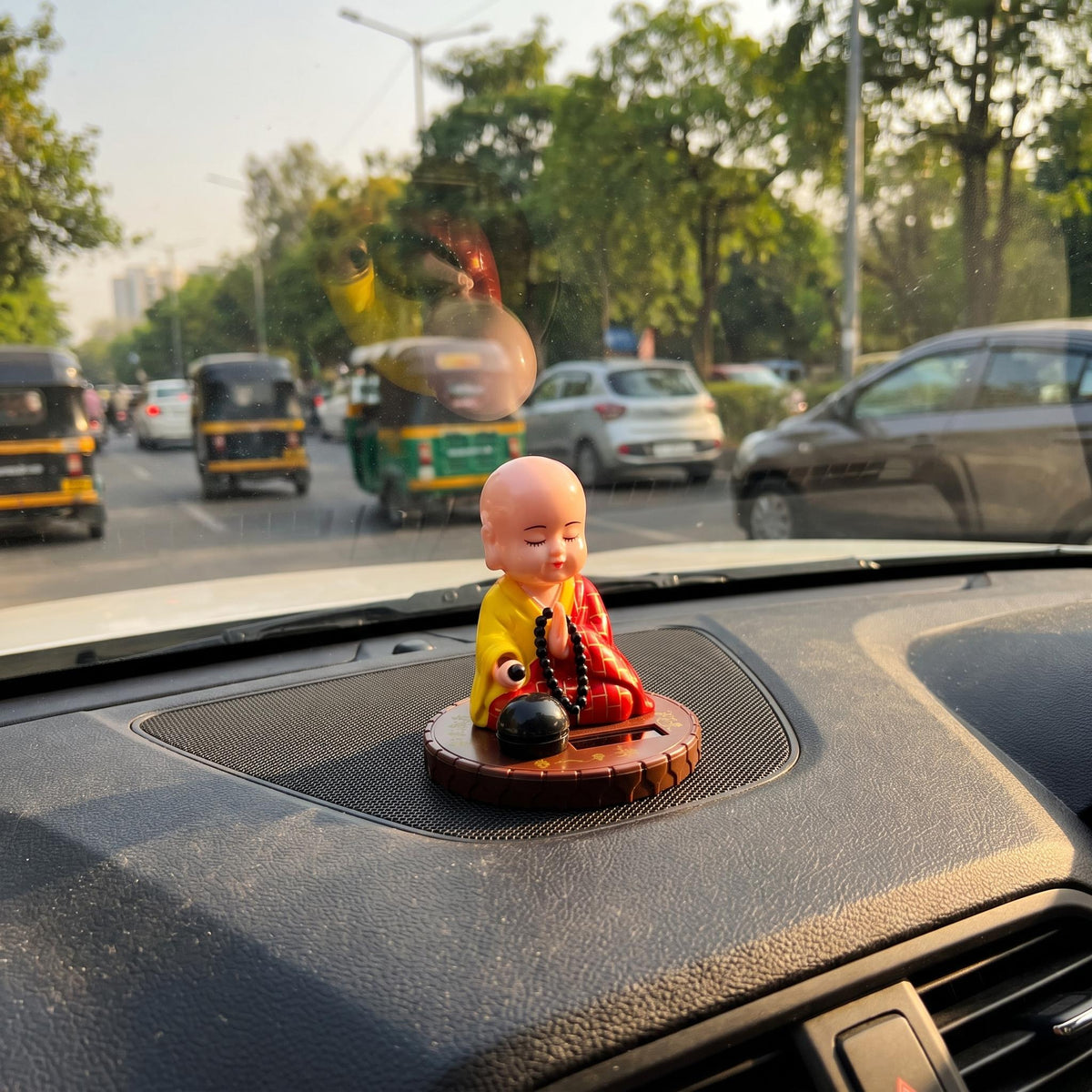 Solar Praying Monk Statue on a car dashboard in traffic